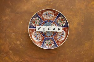 A vibrant decorative plate with the word 'VEGAN' arranged on it, set against a warm, textured background.